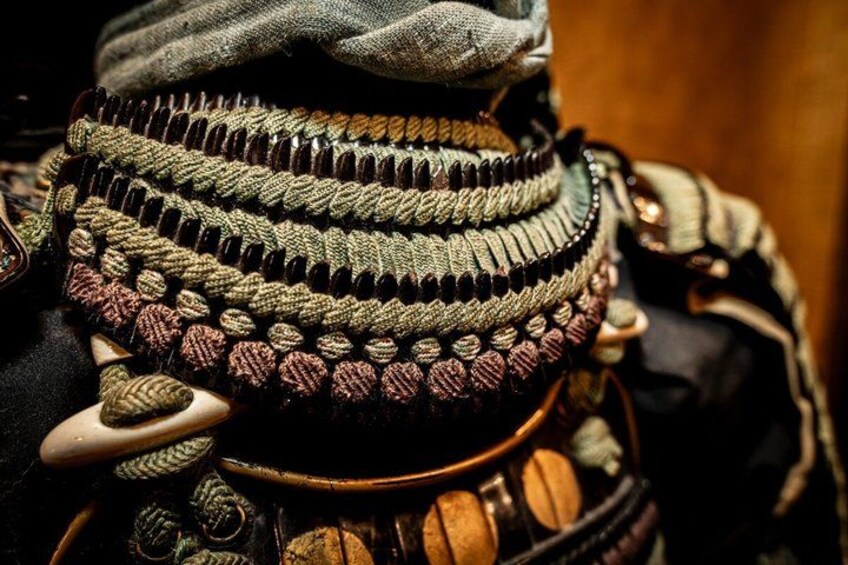 A close-up of a person wearing a layered, textured garment with intricate patterns and multiple accessories. 2