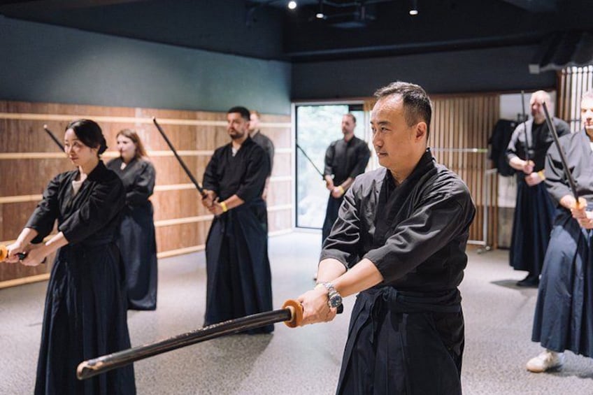 Clase de artes marciales con participantes en uniformes negros practicando con espadas. 5