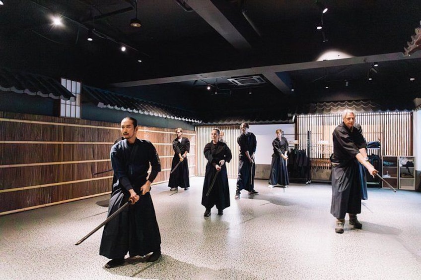 Un grupo de personas con vestimenta tradicional practicando artes marciales en un espacio interior moderno. 4