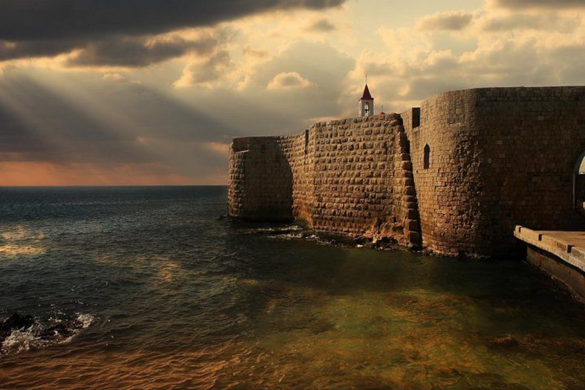 A stone fortress by the sea with a tower, under a cloudy sky. 2