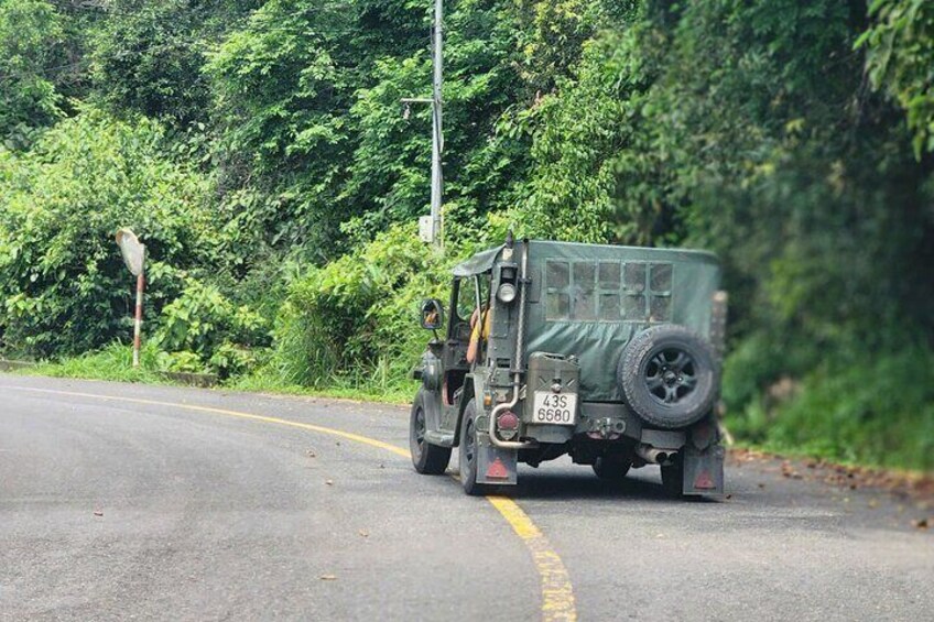 A military vehicle with a spare tire on the back, driving on a road with a yellow line. 5