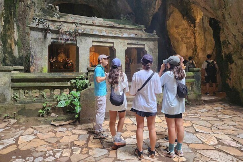 En gruppe turister ved indgangen til et huletempel med stensøjler og et lille helligdom. 2