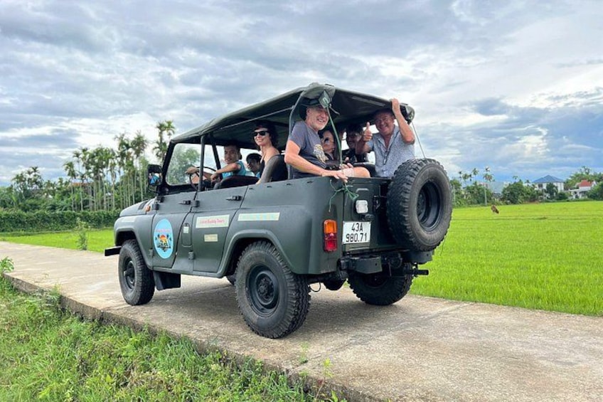 A group of people in a jeep on a paved path with green fields and palm trees in the background. 4