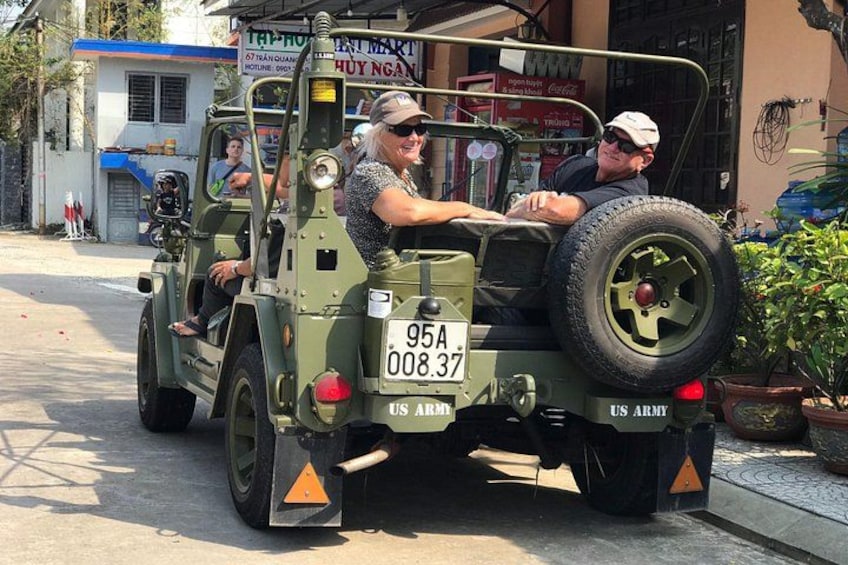 A military jeep with a license plate, a person driving, and another person sitting in the back. 2