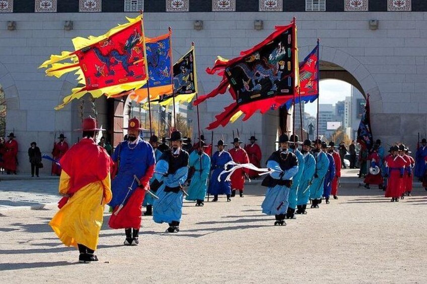 Ein traditioneller Umzug mit Teilnehmern in farbenprächtigen Kostümen, Fahnen und einem steinernen Torbogen im Hintergrund. 5