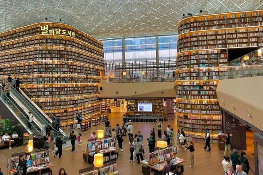 Eine große Innenraumbibliothek mit mehreren Ebenen, Bücherregalen und einer Rolltreppe. 1