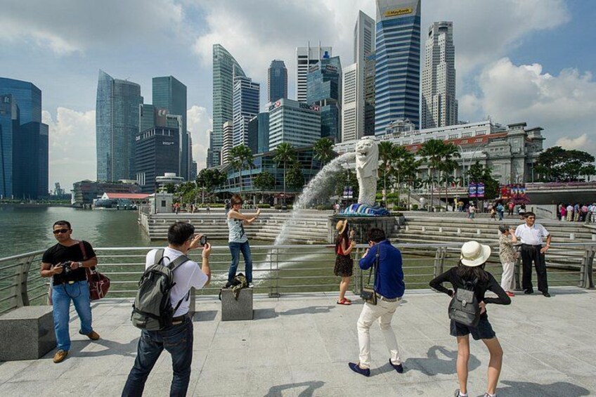 Eine Uferpromenade mit Menschen, die Fotos machen, einem Brunnen und modernen Wolkenkratzern im Hintergrund. 2