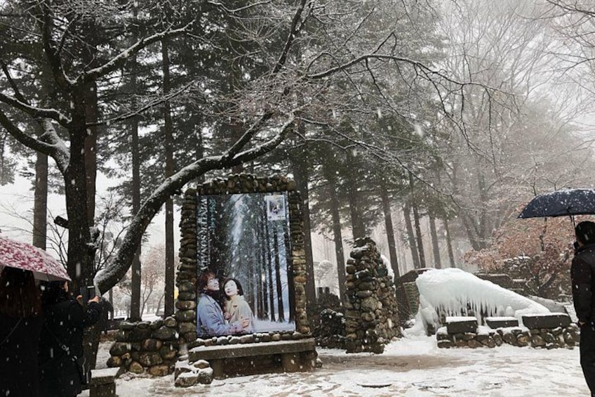 A snowy forest scene with a stone structure, a person under an umbrella, and a snow-covered bench. 5