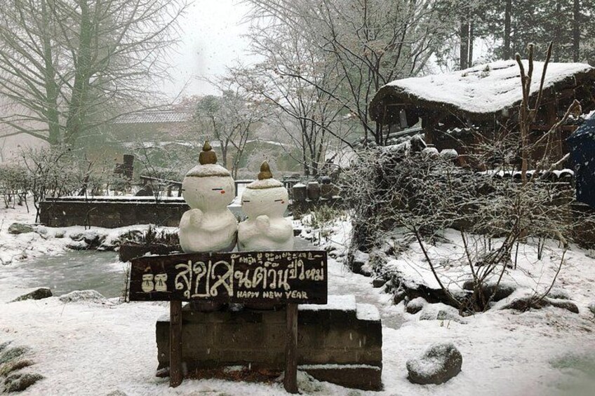 Un paisaje nevado con un letrero de madera que muestra muñecos de nieve y un saludo en un alfabeto extranjero. 4