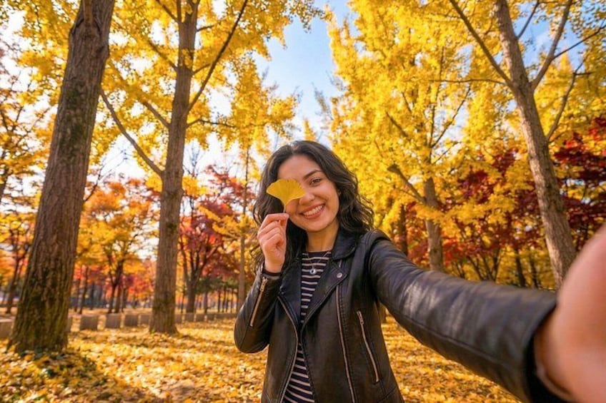 A person taking a selfie in a forest with autumn-colored trees. 2