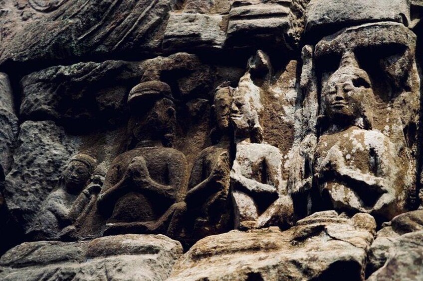 Gamle stenhugninger af siddende figurer, muligvis guddomme eller historiske personer, på en vejrbidt klippeoverflade. 4