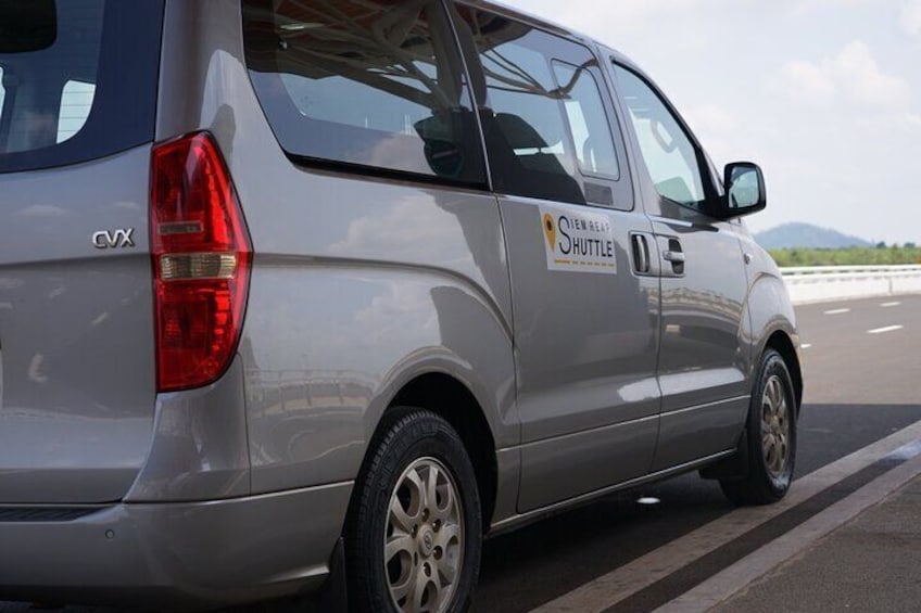 Un minibus argenté, sur lequel on pouvait lire « NEW ENGLAND SHUTTLE », était garé au bord d’une route, avec un ciel dégagé et des montagnes en arrière-plan. 2