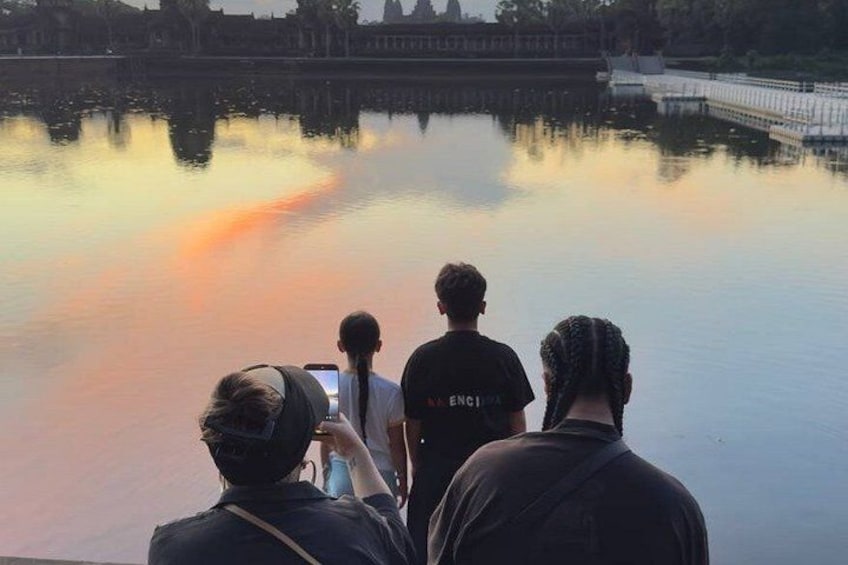 A group of people standing by a calm body of water with a sunset in the background. 5