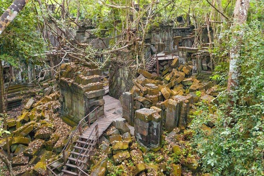 A dilapidated stone structure with a wooden staircase surrounded by overgrown vegetation. 3