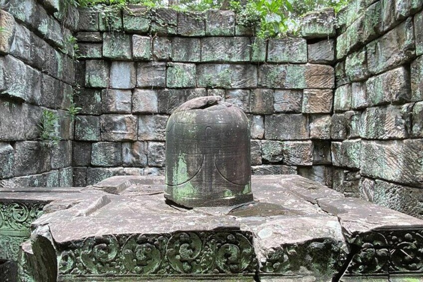 A stone bell on a pedestal with intricate carvings, set against a backdrop of stone walls. 2