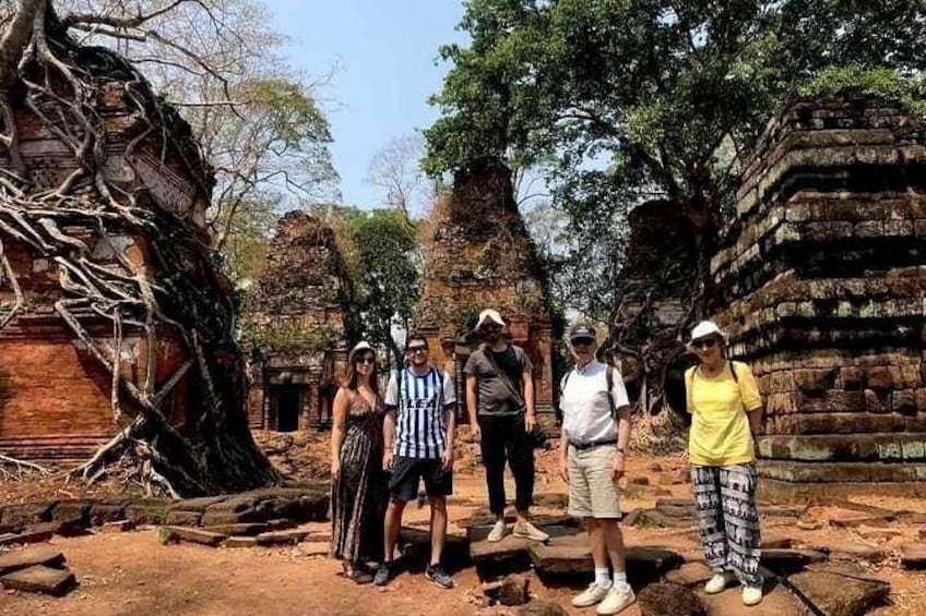 A group of people standing in front of ancient ruins with overgrown trees and stone structures. 5