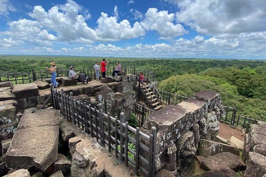 A stone structure with a wooden fence, surrounded by lush greenery and a clear sky. 5
