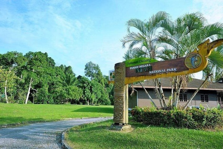 Un panneau indiquant le parc national de Taman Negara, avec des palmiers et un bâtiment en arrière-plan. 2