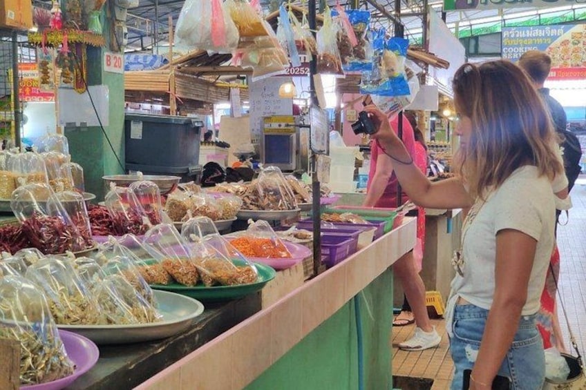Ein Marktstand mit verschiedenen verpackten Waren, eine Person macht ein Foto und ein Fernseher ist im Hintergrund zu sehen. 2