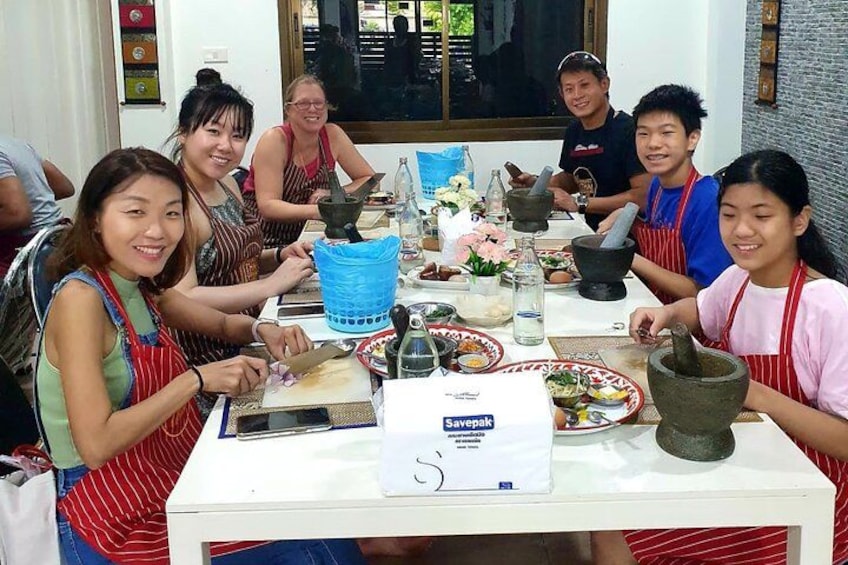 Un grupo de personas sentadas alrededor de una mesa con utensilios de cocina e ingredientes, sugiriendo una clase o taller de cocina. 5