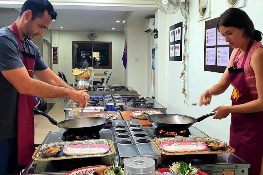 Una cocina con dos personas cocinando. Hay varias estaciones de cocina con sartenes, parrillas y alimentos. 4