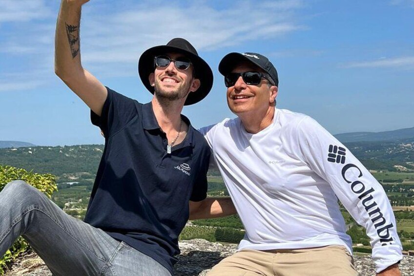 Two people sitting on a rock with a scenic landscape in the background. 1