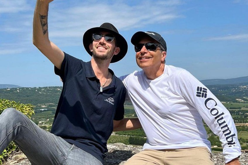 Two people sitting on a rock with a scenic landscape in the background. 1