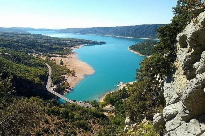 A coastal landscape with a clear blue lake, a sandy beach, and a rocky cliff. 4