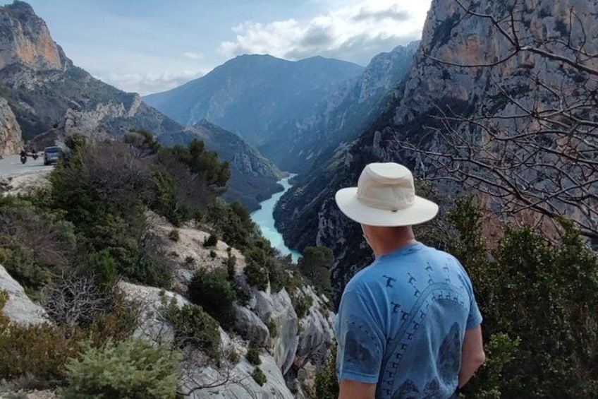 A man in a hat and blue shirt overlooking a canyon with a river. 3