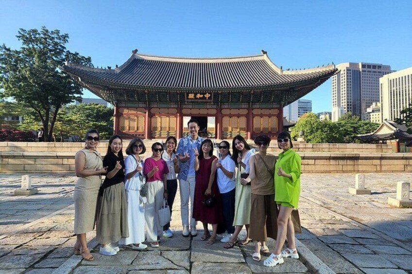 A group of people posing in front of a traditional Korean building with a tiled roof and wooden structure. 5