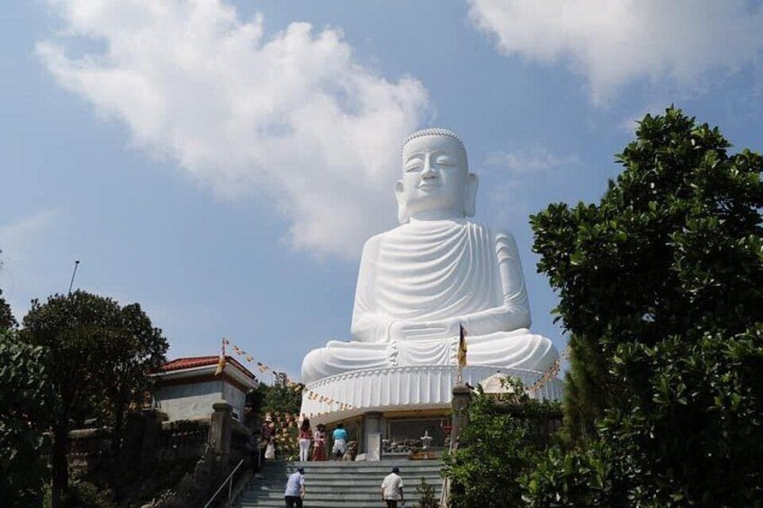 A large white statue of a seated figure, surrounded by trees and a building with a red roof. 4
