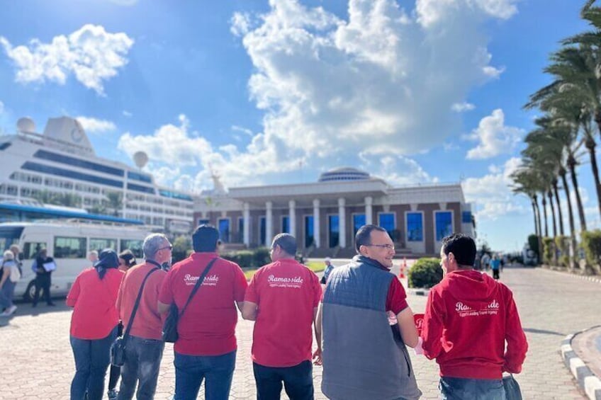 A group of people in red shirts standing in front of a large building with columns and a blue sky with clouds. 4