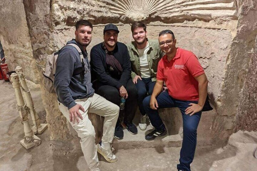 Four people sitting in a cave-like structure with stone walls and a decorative ceiling. 2