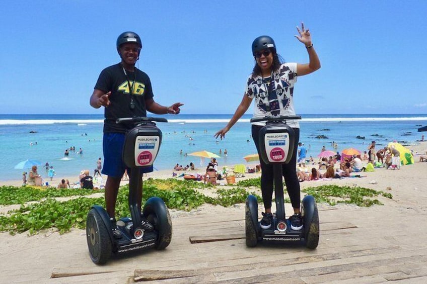 To personer på segways på en strand med oceanen og mennesker i baggrunden. 5