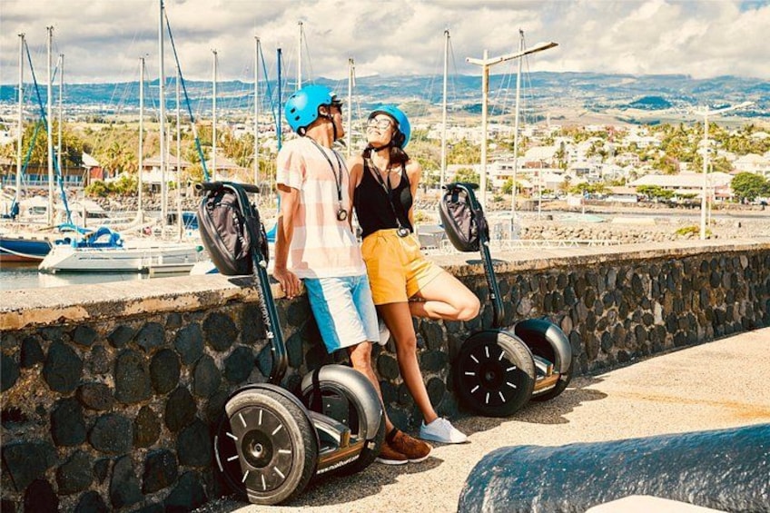 Two people on segways by a waterfront with boats and a stone wall. 1