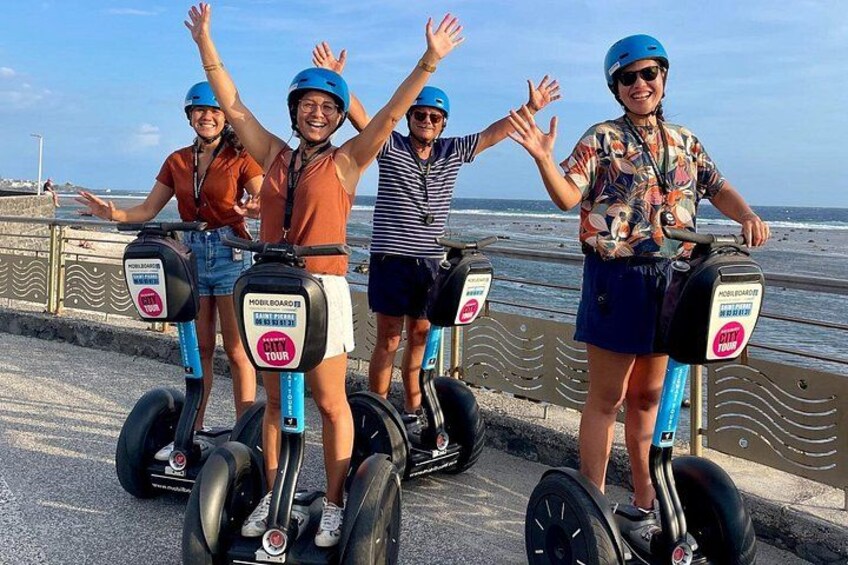 Four people on Segways near a waterfront with a railing and ocean in the background. 3