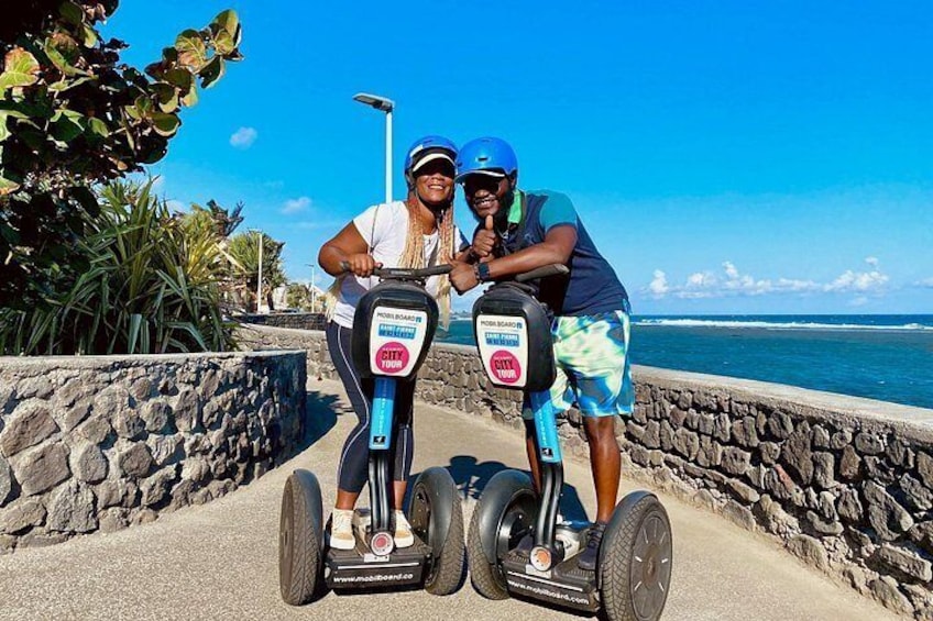 To personer på Segway-hoverboards nær en kyststrækning med en stenvæg og hav i baggrunden. 3