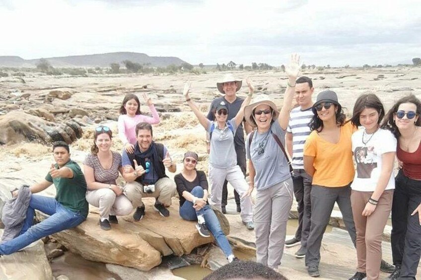 A group of people posing on a rocky outcrop with a desert landscape in the background. 5