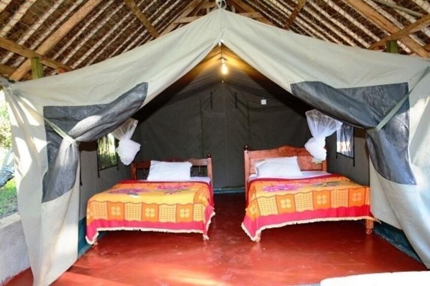 A thatched-roof tent with two beds, each with a colorful bedspread. 4