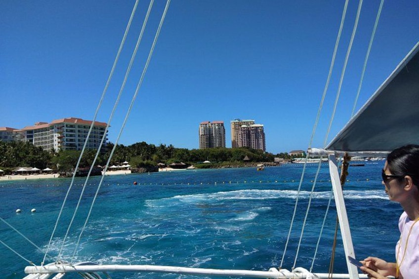 A sailboat on a clear blue sea with buildings in the background. 3