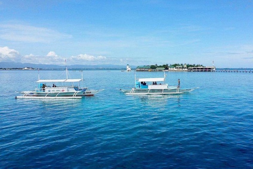 Two boats on calm blue water with a distant island and lighthouse. 1