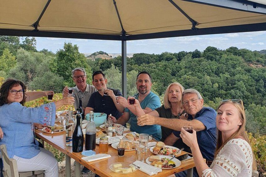 Un grupo de personas sentadas en una mesa al aire libre, con comida y bebidas, rodeadas de follaje. 3