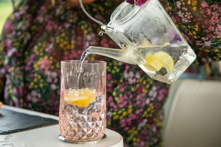 A person pouring a clear liquid from a pitcher into a glass with ice and a slice of lemon. 2