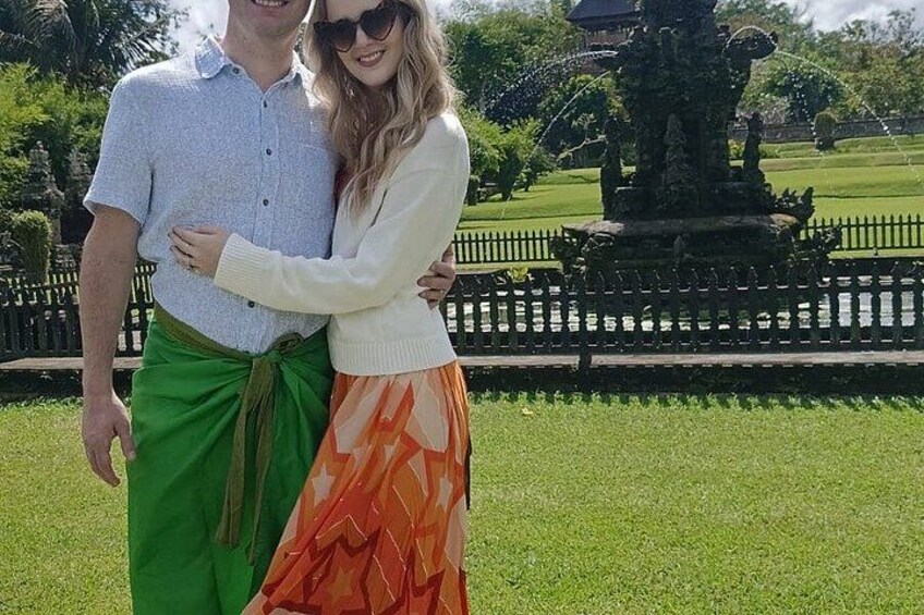 A couple embracing in a park with a fountain and a fence in the background. 4