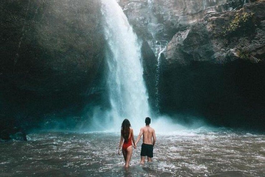 Two people walking towards a waterfall in a rocky area. 1