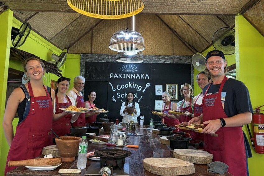 Una escuela de cocina con participantes usando delantales, preparando alimentos con utensilios y varios ingredientes sobre una encimera. 1
