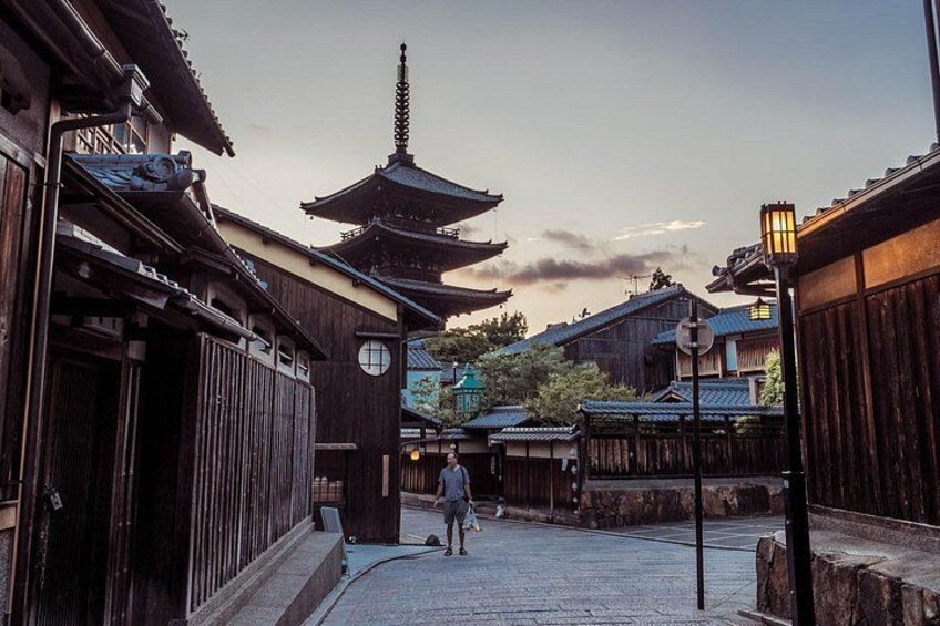 En traditionel japansk gade med træbygninger, en pagode og en person, der går forbi. 3