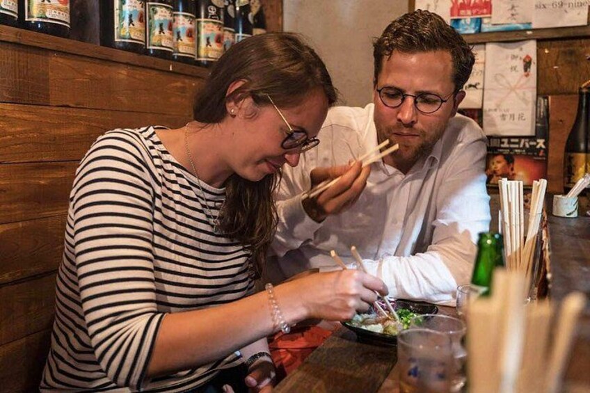 Zwei Personen essen in einem Restaurant mit Stäbchen, einer Flasche und einer Speisekarte auf dem Tisch. 4