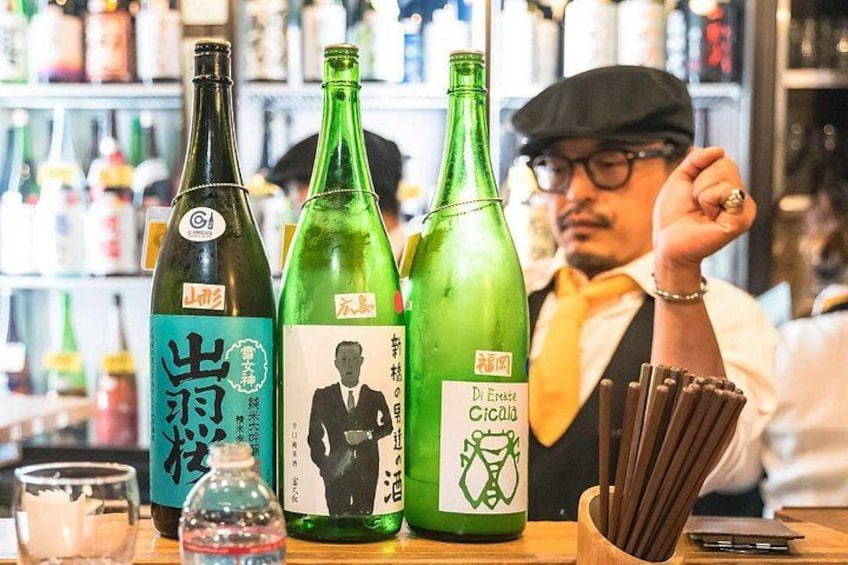 Drei grüne Flaschen mit Etiketten, ein Glas und eine Wasserflasche auf einer Bar. 3