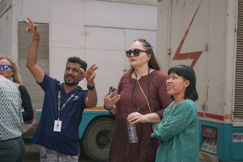 A group of people standing outdoors, some holding drinks, with a truck and a building in the background. 2